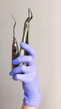 Extreme close up of dentist holding extraction forceps and stainless steel root tip elevator. Surgical instruments prepared for tooth removal procedure highlighting precision control 
