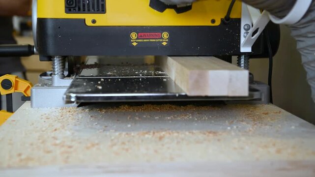 A wood plate passing through the thickness planer machine in a carpentry workshop. Woodworking process, furniture preparation, handmade craftsmanship, carpentry studio.