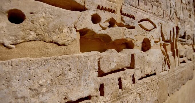 Closeup of ancient Egyptian hieroglyphic inscriptions with cartouches and bird symbols carved in sandstone wall at Medinet Habu temple in Luxor Egypt, detailed royal text.