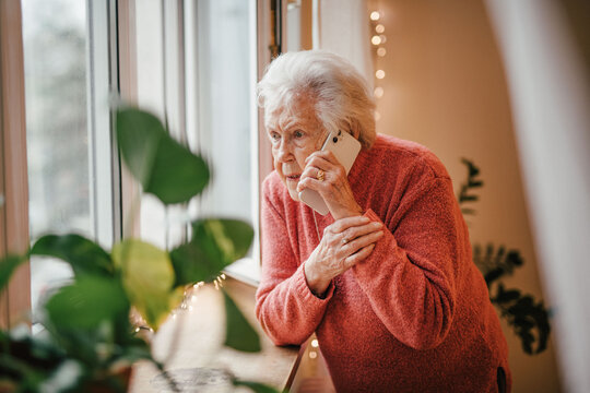 Old woman standing by window, making phone call.