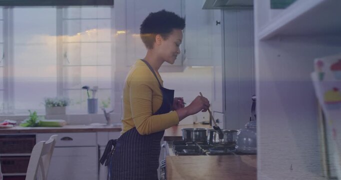 Home cook starting stirring motion at gas stove, lens flare crossing cook and pots, preparing meal