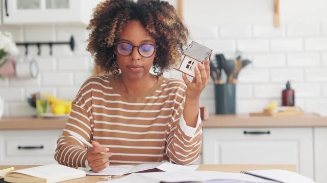young African American girl holds mock up of house in her hands carefully examines it, making notes in notebook. business person is architect working house construction project. high quality 4k video