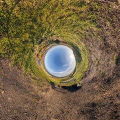 creative tiny planet photo of a rural landscape with dirt road, green fields, and cloudy sky forming a circular world.