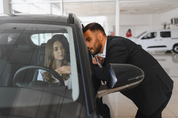 Car salesman talking with woman inside new vehicle