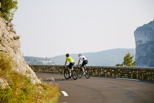 Two Cyclists Riding Curved Mountain Road