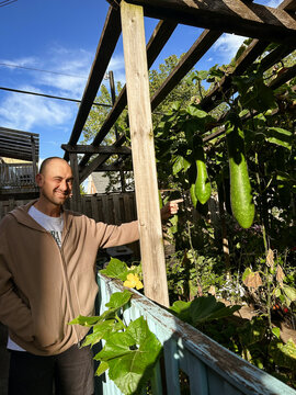 Man Points at Hanging Vegetables in Garden During Afternoon Light