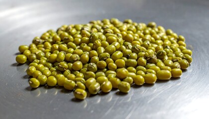 A close-up shot of a heap of small, round, green seeds, resting on a reflective, metallic surface. The light accentuates the texture
