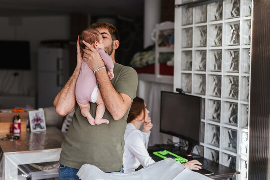 A man changes his daughter's clothes while his wife works at home.