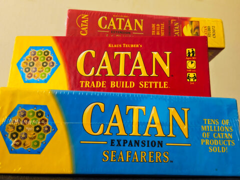 A stack of CATAN board games, featuring the original edition and extension and expansion editions. Editorial Use Only.