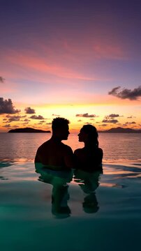Romantic tropical getaway. Silhouette couple watching the vibrant sunset over the ocean from an infinity pool. Use for luxury travel advertising. Vertical. Video. Portrait Orientation.