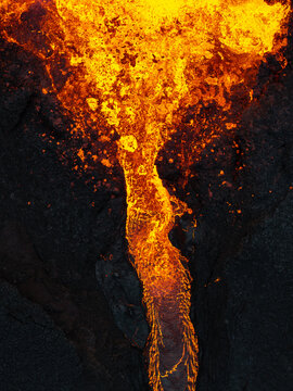 Aerial view of molten lava cascading down rugged, blackened terrain, creating a mesmerizing dance of fire and earth, Iceland.