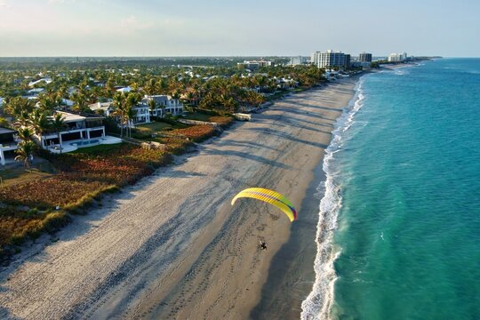 Aerial view of a parasail soaring above the shore, the beach with the buildings and lush vegetation in the background, Jupiter, Florida, United States.
