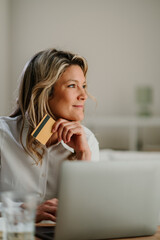 Woman using a credit card and laptop for online shopping, contemplating her next purchase or...