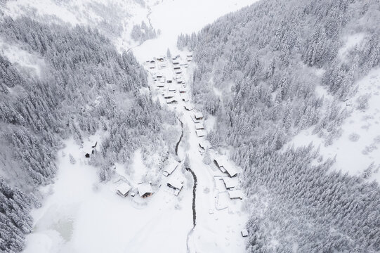 Aerial view of a snow-laden village nestled between frosted, evergreen trees, a stark white blanket covering everything in sight, Vouvry, Valais, Switzerland.