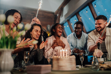 Obraz premium Diverse friends celebrating birthday party, surprising woman with cake, candles, and sparklers, feeling joy, emotion, and happiness