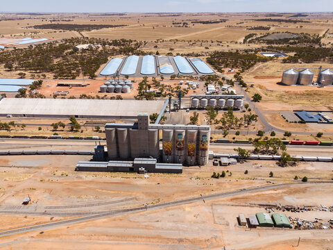 Aerial view of grain silos casting long shadows across the arid landscape, railway lines bisecting the scene, Merredin, Western Australia, Australia.