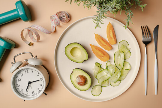 Creative flat lay composition with plate, alarm clock, knife, fork, dumbbell and measuring tape on pink background. Intermittent fasting, ketogenic, diet concept. top view, copy space.
