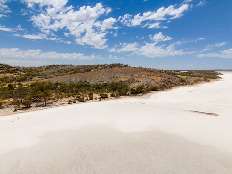 Aerial view of expansive, sun-drenched salt flats meet the rugged, ochre-toned landscape under a bright azure sky, Lake Campion Nature Reserve, Western Australia, Australia.