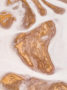 Aerial view of abstract patterns of golden land surrounded by a sea of white, creating a striking contrast of warm and cool tones, Lake Campion, Western Australia, Australia.