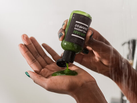 Woman squeezing shampoo from bottle in shower 