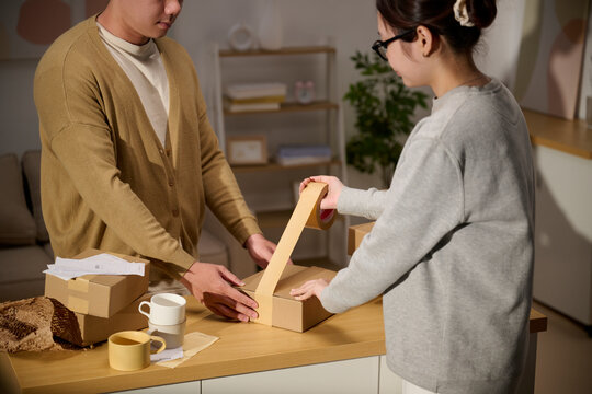 Couple packing cardboard boxes together at home for shipping