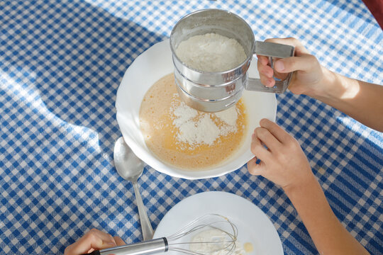 Child's hands add flour to pancake batter