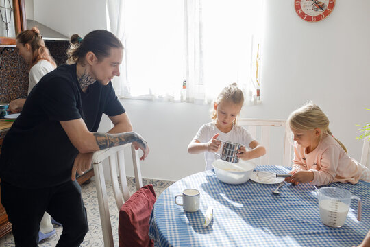 Children and father sifting flour in the kitchen