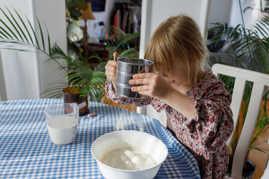 Little girl sifting flour in the kitchen