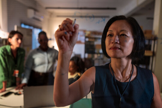 Woman writing on glass board with team in background.