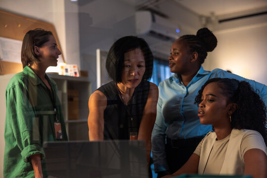 Diverse women collaborate, looking at a laptop screen.
