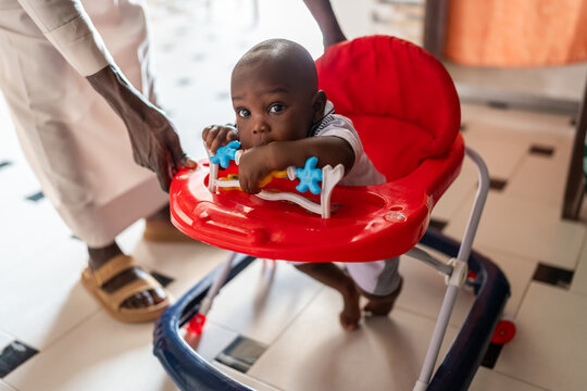African infant boy learning walking in red baby walker
