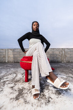 African woman sitting on a stool wearing hijab and striped outfit