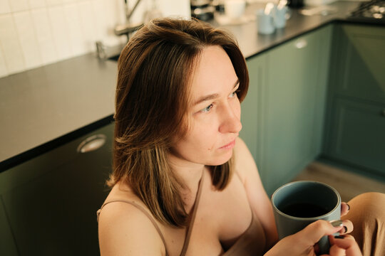 Closeup portrait of sad woman with coffee cup sitting at the kitchen 