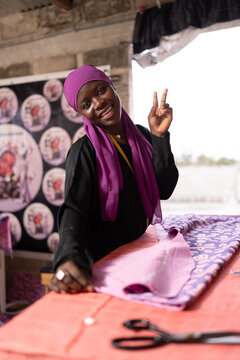 Smiling woman making peace sign working on fabric