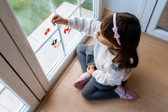 Little girl decorating home window for Christmas holiday