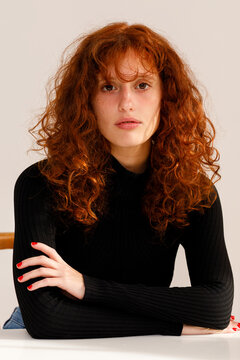 Red Haired Person Sitting at a Table Looking Into the Camera