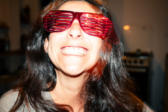 Woman wearing red party sunglasses smiling at camera with direct flash