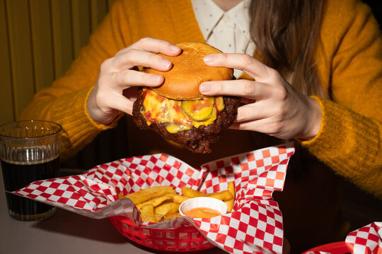 Hands Holding a Burger With Fries and Drink on a Table