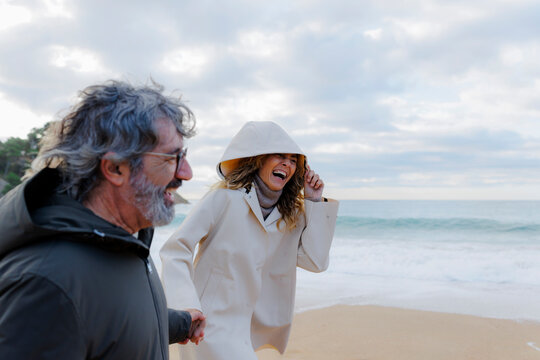 Mature couple laughing walking along ocean beach