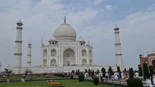 Cinematic wide shot of the Taj Mahal monument with tourists walking in the garden under a cloudy sky in Agra, India