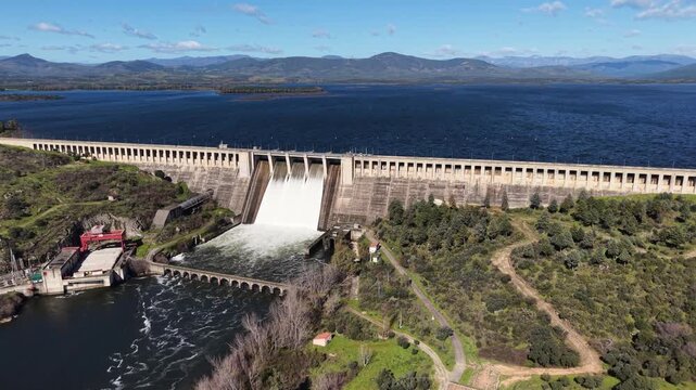 Aerial view of water gushing from the dam contrasting with the still lake water, surrounded by green vegetation, Extremadura, Spain.