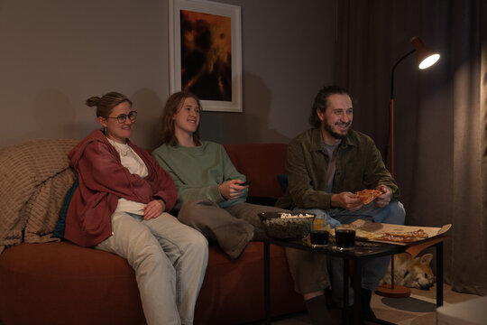 Family watching TV and eating pizza together at home