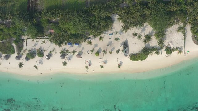 Directly above aerial view of a tropical Thoddoo beach showing a wrecked wooden boat, palm shadows, sun umbrellas, people resting on white sand, and vibrant ocean water.