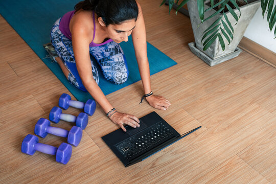 Woman following online workout at home with laptop and dumbbells