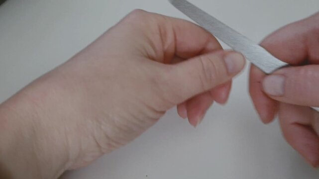 Woman filing fingernail on white table