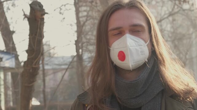Caucasian Man Outdoors Wearing Protective Mask, Long Hair Catching Light, Scarf Layered, City Street. Bad Urban Ecology Air, Smog. Protection Mask for Health. Eco Volunteer, FFP3 Respirator, Safety