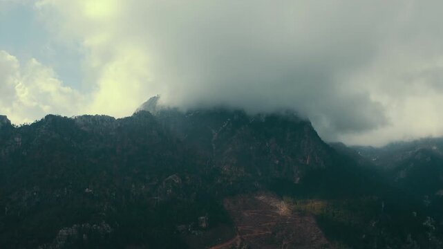 Backward moving drone; aerial panoramic view over misty Taurus Mountains peaks with clouds and dense pine forests, capturing a slow pull back.