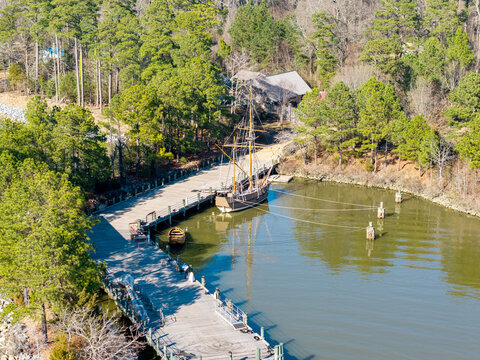 Colonial-era merchant ship replica, the Godspeed, docked at the wooden pier of the Jamestown Settlement living history museum on the James River. Aerial view.