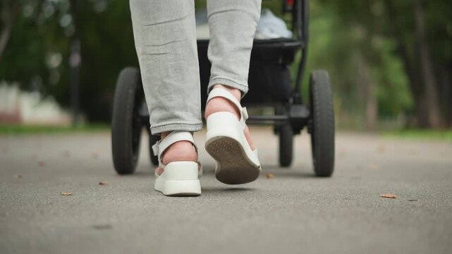 Closeup white mother feet walking stroller on sunlit park pavement, casual sneakers scuffing ground, tender parenting routine, calm afternoon, urban lifestyle decree captured in lowangle frames