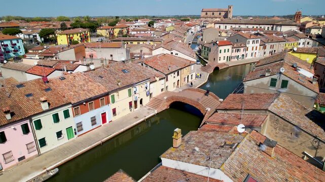 Comacchio aerial 4k low flight over narrow canals with flying pigeons in Italy. Colorful houses and brick bridges of Little Venice in Emilia Romagna. Scenic water canal landscape scenery
